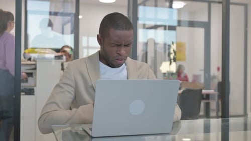 Coughing African Businessman Using Laptop in Office