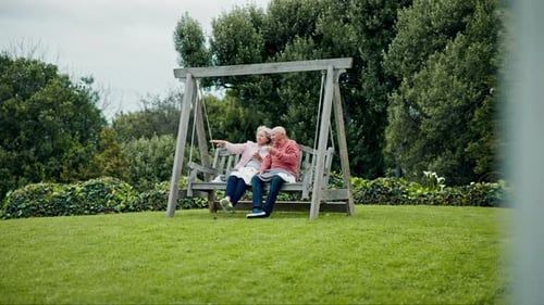 Senior couple on swing in garden with love, conversation and bonding with trees, grass and care
