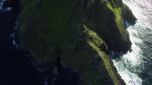 Dramatic aerial view of massive, dark green sea cliffs and crashing waves