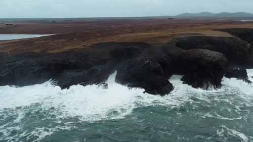 Aerial View: Waves Crashing on Rugged Coastline