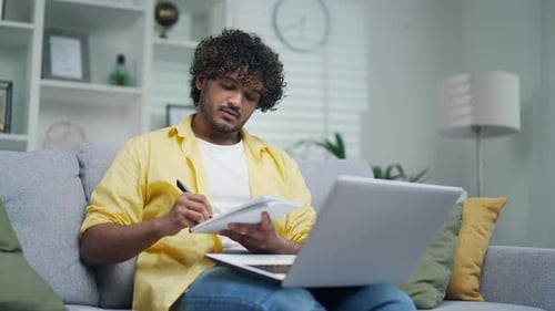 Man Working on Laptop, Taking Notes at Home