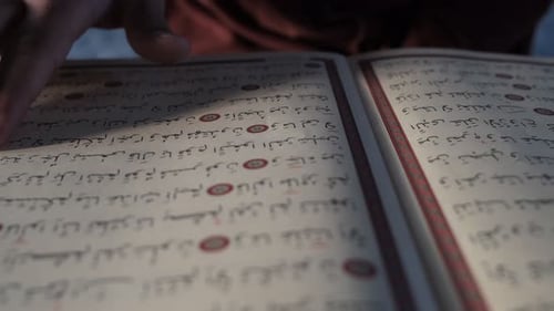 Mann liest das religiöse Buch des Islam, indem er dem Koran mit dem Finger folgt, religiöses Buch mit