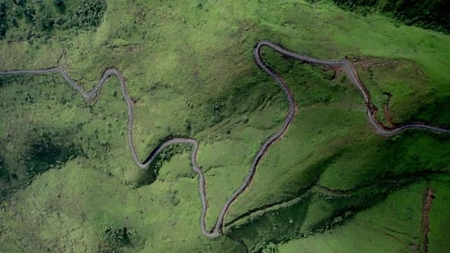Drone footage of a winding mountain road cutting through lush green hills.