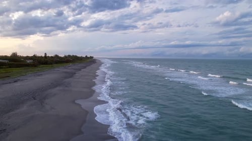 moody weather beach day as drone flys along ocean crashing into shore