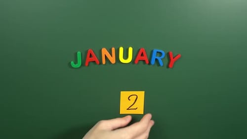 Hand sticking a sticker 2 January calendar day on school board. 2 date of January. Second day