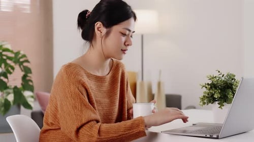 Young modern Asian woman works from home with laptop computer in living room.
