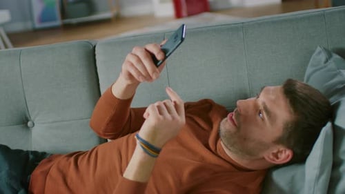 Man Lying on Couch Using Mobile Phone Indoors
