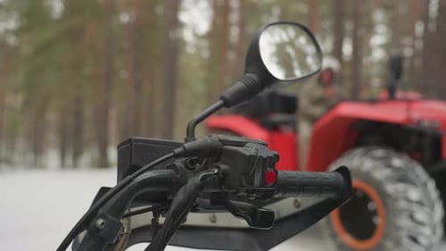 Red ATV Blurred Among Snowy Pine Trees with Focus on Controls Closeup of Glove Gripping ATV Handle
