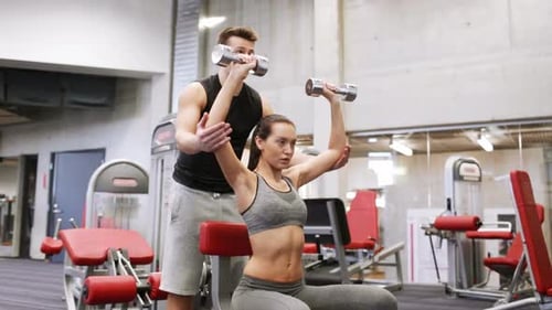 Young woman and personal trainer flexing muscles in gym weightlifting workout