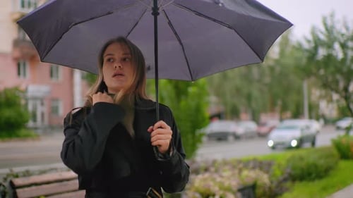 Female with Long Hair Wearing Black Coat Standing Under Umbrella on City Sidewalk