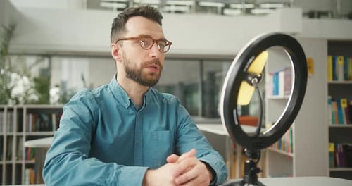 Bearded Man Records Video Greeting Channel Guests in Library