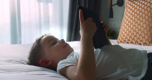 Joli petit garçon souriant utilisant la technologie de tablette numérique allongé seul sur la chambre