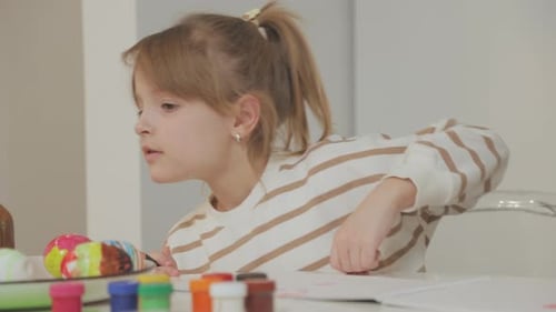 Adorable daughter in striped sweater draws pictures with colored pencils. Close-up.