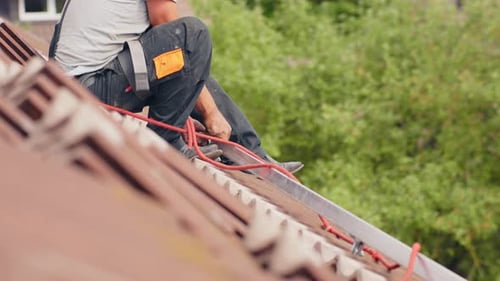 Profile low angle view of technician installing solar panel on roof, static
