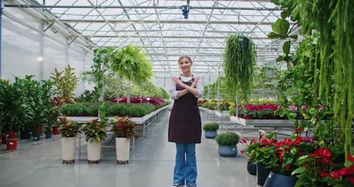 Camera Moving Closer to Cute Caucasian Woman Standing in Middle of Long Greenhouse Crossing Her