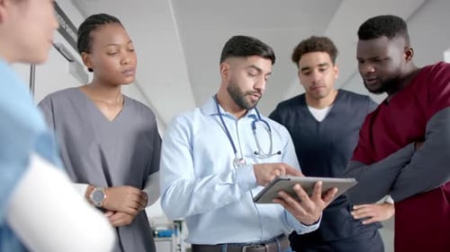 Diverse male and female doctors discussing work using tablet in hospital corridor, slow motion