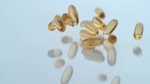 Golden Vitamin Capsules Falling on Reflective Surface