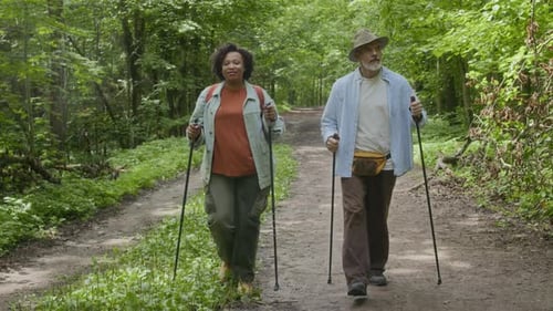 Mature Travelers with Hiking Poles Jogging in Forest Park