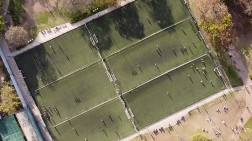 Aerial top-down rising directly above soccer players on row of football training fields
