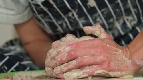 A female potter works on a potter's wheel, making a ceramic pot from clay in a pottery workshop.