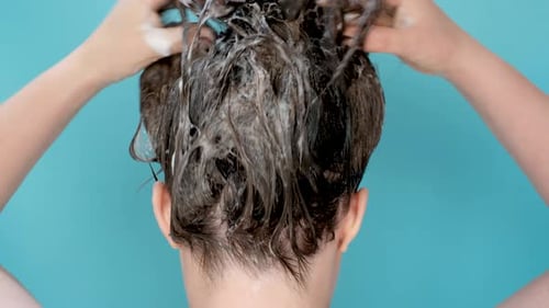 A woman washes her hair with shampoo on mint background, rear view.