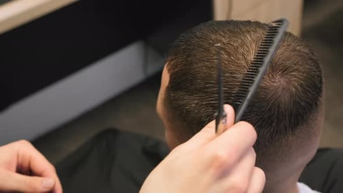 Barber Cuts Client Hair with Comb Holding Scissors in Shop