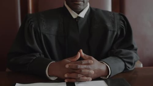 Judge in Robe Sits at a Wooden Table