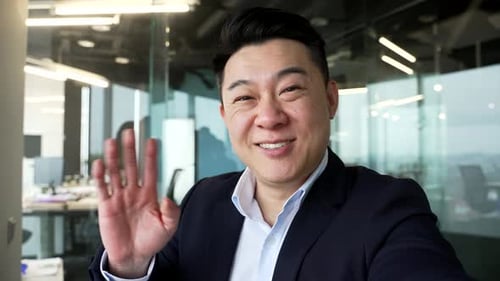 POV Smiling asian businessman talking on a video call using phone in modern office.
