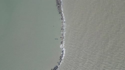 Vue aérienne de petites vagues de mer s'écrasant contre une barrière, avec de l'eau des deux côtés. Le capitaine de la scène