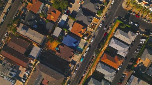 Flying over the roofs and streets of sunny Los Angeles. Numerous cars stand and move by the roads