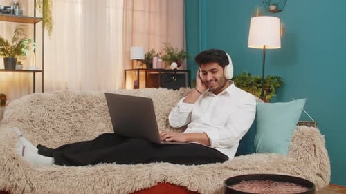 Man Relaxing on Couch Using Laptop and Headphones
