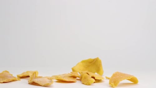 Dried Mango Slices Falling onto White Surface
