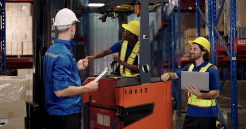 African adult male forklift operator gives thumbs up while communicating with two colleagues holding