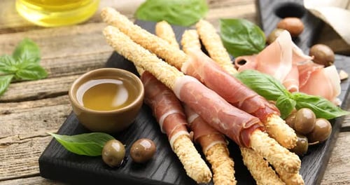 Grissini breadsticks with prosciutto, olives and honey on wooden table, spinning