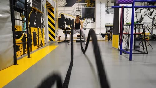 Young Muscular Sportsman Training with Battle Ropes at Modern Gym Strong Sporty Man Exercising in