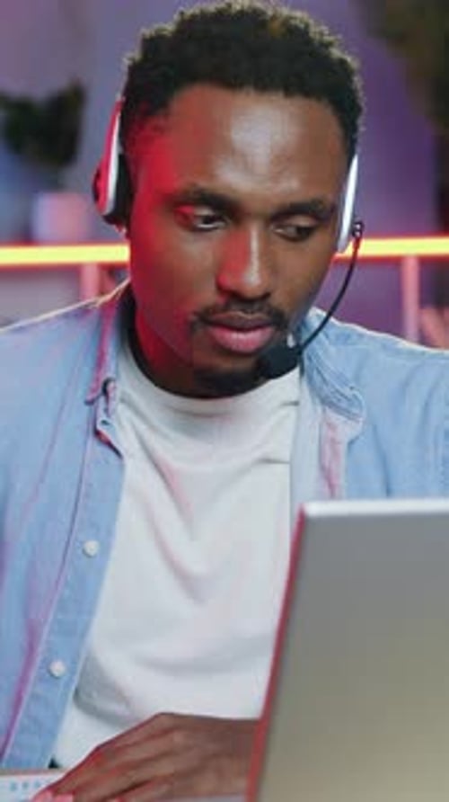 Focused Man Works on Laptop Wearing Headset Indoors