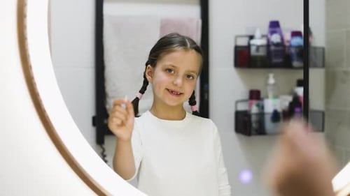 Young Girl wiggling Loose Tooth in Bathroom Mirror