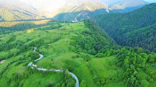 A Road Passes Hills Covered with Spruce Forests and Meadows Against a Cloudy Sky