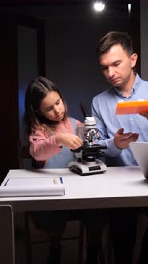 Girl and Man Using Microscope Together at Table