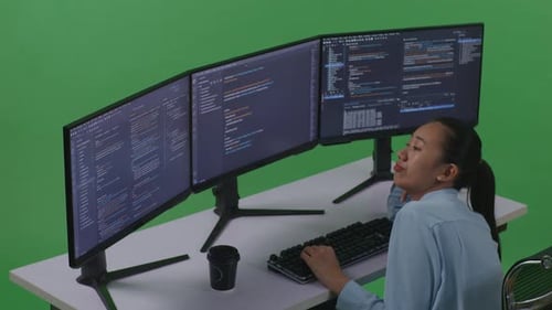Side View Of Bored Asian Woman Developer Write Code With Multiple Computer In Green Screen