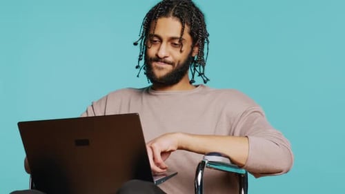 Man in Wheelchair Chatting with Friend Over Internet Videocall Using Laptop