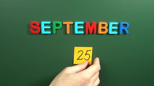 Hand sticking a sticker 25 September calendar day on school board. 25 date of September. Twenty