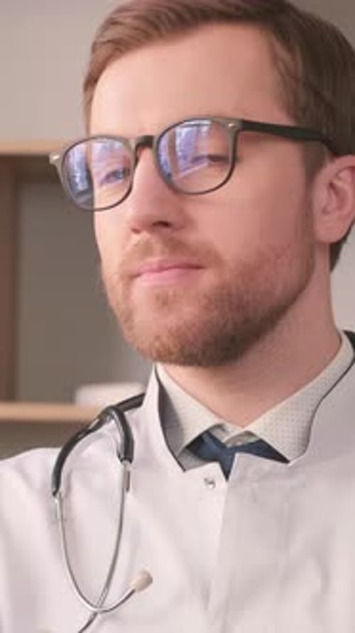 A Young Intern Doctor in a White Coat is Looking at the Camera and Smiling Vertical Video