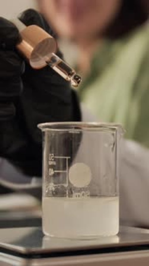 Femme versant de l'huile essentielle dans un bécher pour la formulation du parfum