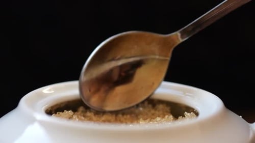 Der Löffel nimmt Zucker aus der Zuckerdose auf