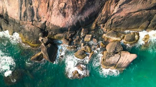 Aerial View of Turquoise Waves Smashing Rocky Coastline Generating Foaming White Water Against