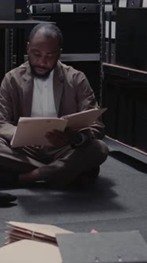 Adult Reviews Documents Seated on Floor in Storage Room