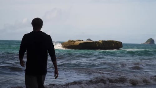 Man Standing on a Beach Looking at the Ocean