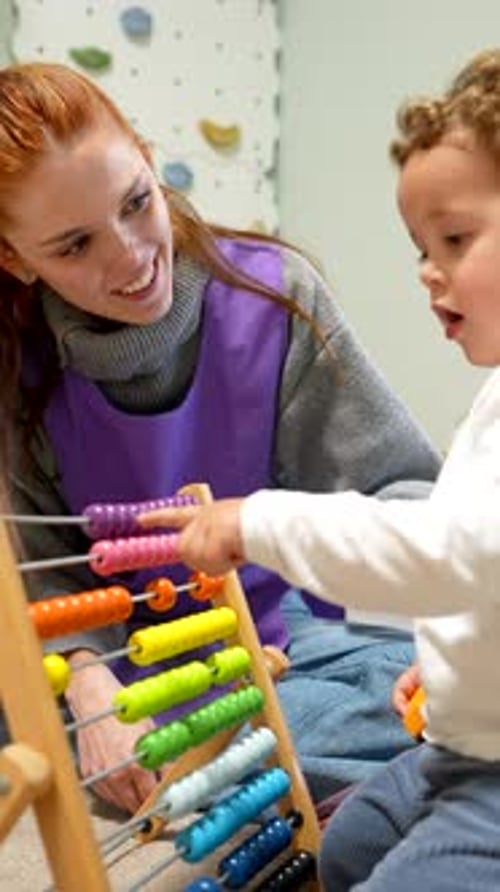 Maestra de guardería enseñando colores a un niño pequeño con un ábaco