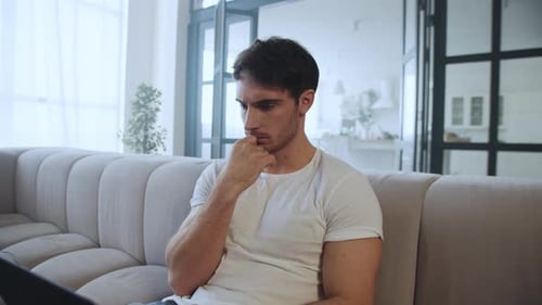 Thoughtful Man Works on Laptop While Relaxing at Home